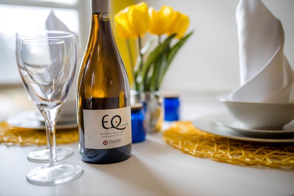 A bottle of wine, a glass, and a vase with yellow flowers on a table.