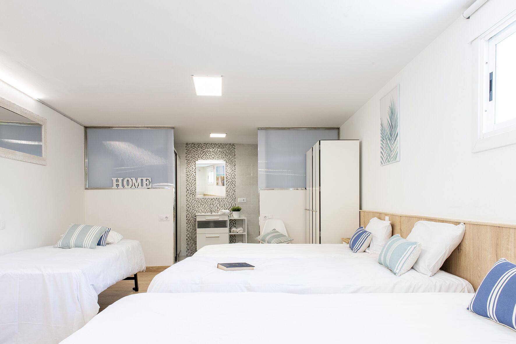 Ein modernes Schlafzimmer mit zwei Einzelbetten, einem großen Spiegel, einem Kleiderschrank und einem Badezimmer mit Dusche und Waschbecken.