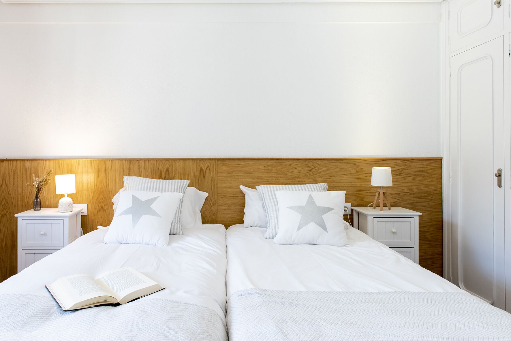 Un lit double avec deux tables de chevet, chacune équipée d’une lampe. On trouve deux oreillers ornés de motifs en forme d’étoiles et un livre sur le lit.