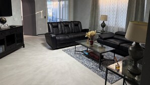 A modern living room with a black leather sofa, a glass coffee table, and a chandelier. - Find Tranquility: Escape Life’s Chaos in a Soul-Soothing Oasis Vacation Home (Kissimmee)