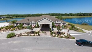 A two-story building with a covered entrance, surrounded by a landscaped driveway and a body of water in the background. - Find Tranquility: Escape Life’s Chaos in a Soul-Soothing Oasis Vacation Home (Kissimmee)