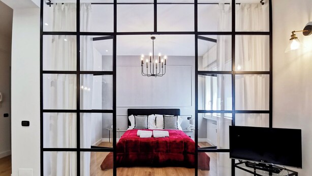 Un dormitorio moderno con una cama grande, un televisor sobre un mueble bajo y una araña.
