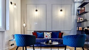 Una sala de estar moderna con un sofá, dos sillones azules, una mesa de centro y una estantería.