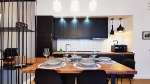 Una cocina moderna con armarios oscuros, una mesa de comedor de madera dispuesta con platos y vasos, y lámparas colgantes arriba.