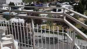 Uma varanda com cadeiras de plástico branco, guarda-corpo de metal e vista para uma marina com barcos e edifícios ao fundo.