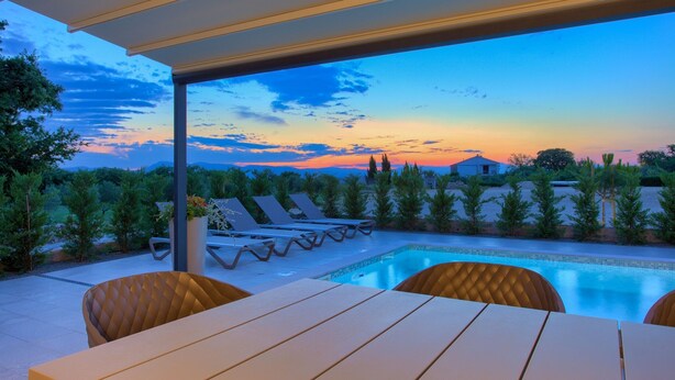 A poolside area with lounge chairs and a table, overlooking a swimming pool and a scenic sunset view. - Villa Elegant with heated pool (Kvarner - Vrh) (Vrh)