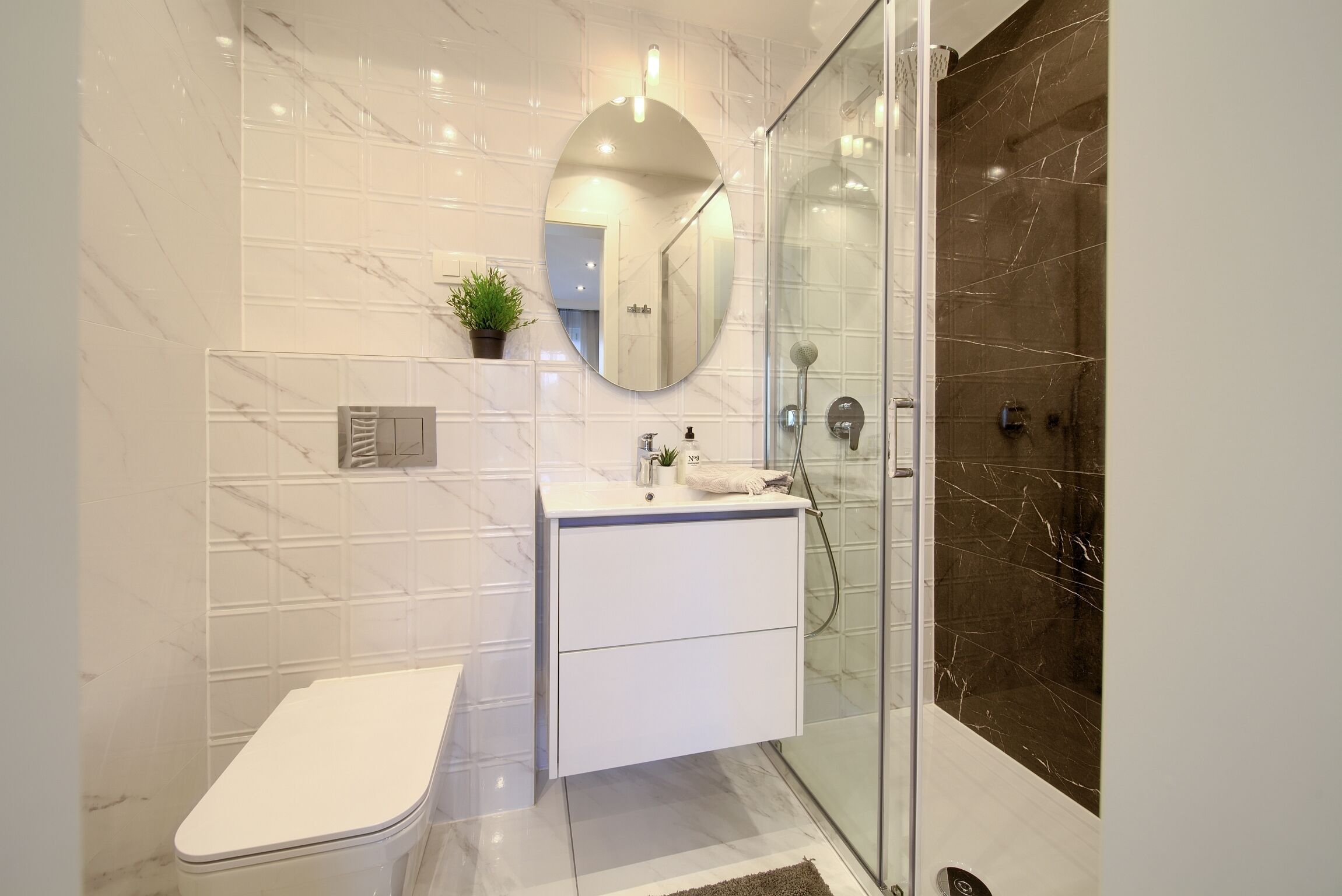 Ein modernes Badezimmer mit Duschkabine aus Glas, einem weißen Waschtisch mit Spiegel und einer Toilette.