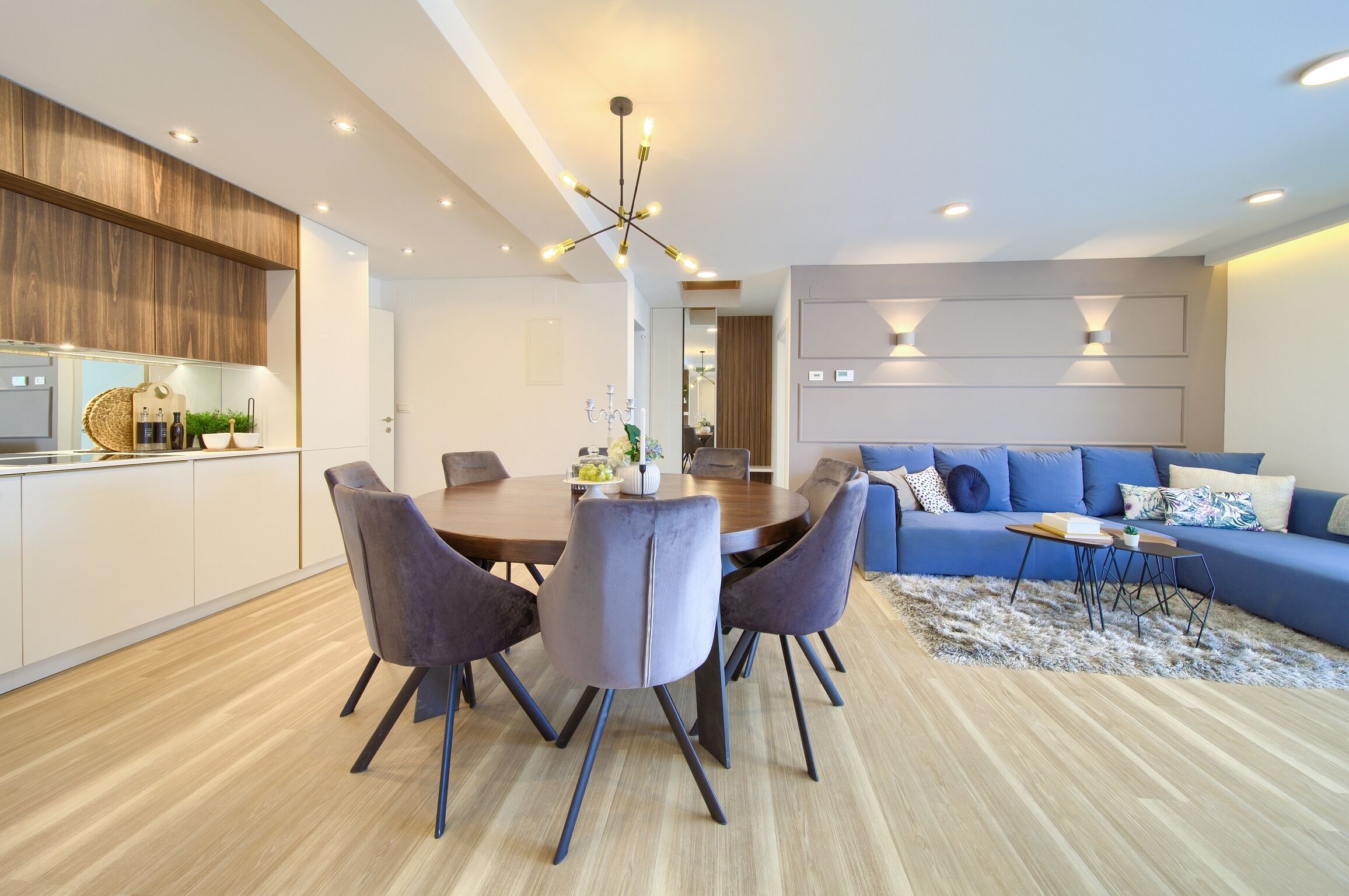 A modern kitchen with a dining area, a blue sofa, and a chandelier.