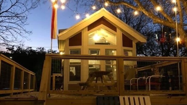 Une cabane en bois dotée d’un balcon, de guirlandes lumineuses et d’un drapeau.