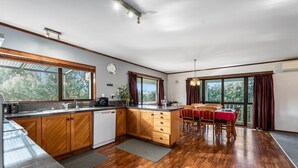 Une cuisine spacieuse avec des meubles en bois, un lave-vaisselle intégré et un coin repas agrémenté d’une nappe rouge.