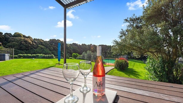 Une table en bois, une bouteille de vin et deux verres sont posés sur une dalle de marbre, le tout installé à l’extérieur, avec vue sur une pelouse verdoyante et des arbres.