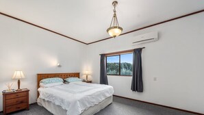 Une chambre à coucher avec un lit, deux tables de chevet avec des lampes, une fenêtre avec des rideaux et un appareil de climatisation fixé au mur.