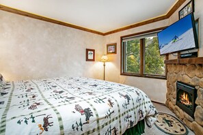 Quarto com cama, lareira, televisão e janela com vista para árvores.