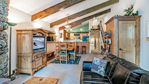 A cozy living room with a wooden TV stand, a leather sofa, and a dining area with wooden chairs and a table. - Beaver Creek West 4bd/4ba free Ski shuttle The Perfect Mountain Nest (Avon)