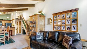 A cozy living room with a black leather couch, wooden shelves, and a wall decorated with framed photographs. - Beaver Creek West 4bd/4ba free Ski shuttle The Perfect Mountain Nest (Avon)