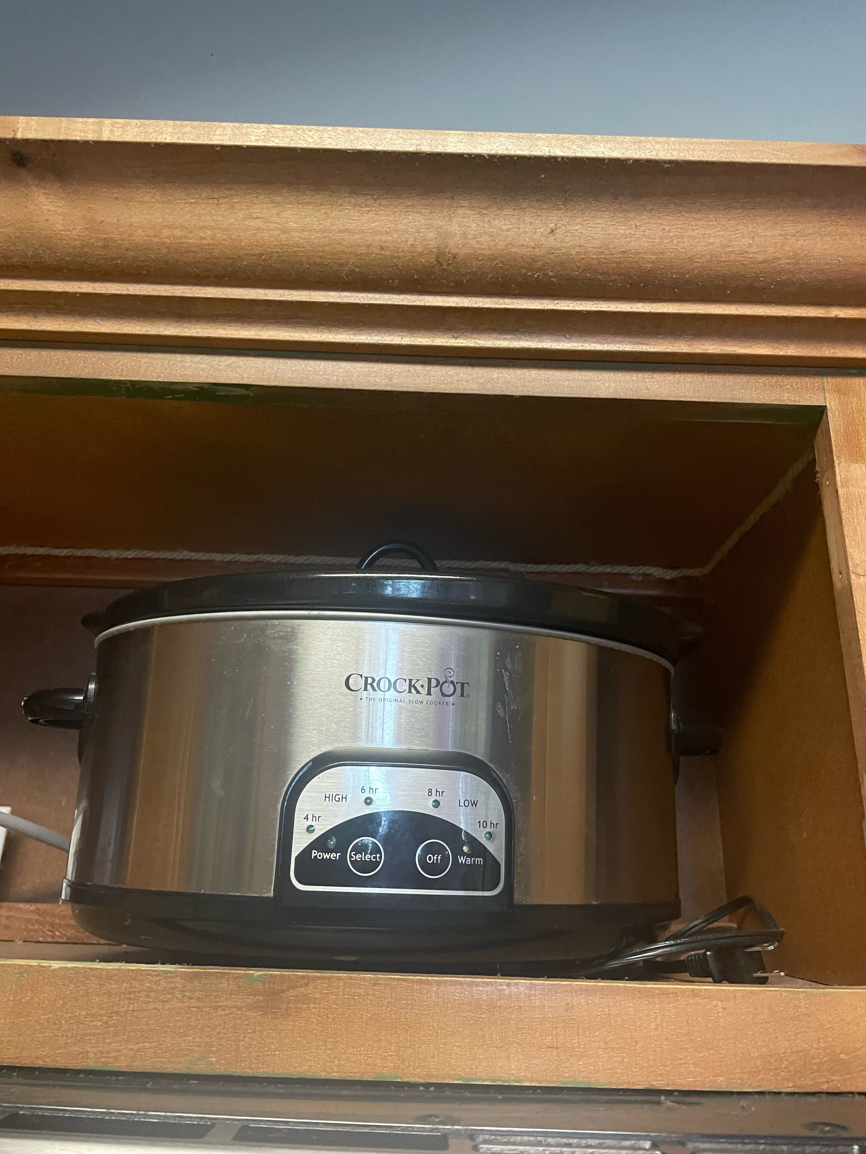 A stainless steel Crock-Pot slow cooker inside a wooden cabinet.