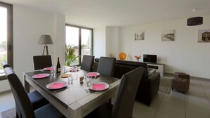 Un coin repas avec une table dressée pour quatre personnes, des chaises, une lampe, un canapé, un téléviseur et des œuvres d’art accrochées au mur.