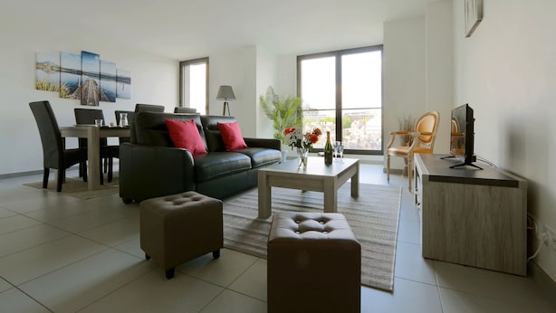 Un salon moderne comprenant un canapé, une table basse, un pouf, une table à manger, des chaises et un meuble pour la télévision.