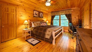 Ein gemütliches Schlafzimmer in einer Blockhütte mit einem Bett, Nachttischlampen, einem Fenster und einem Deckenventilator.