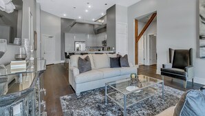 A modern living room with a glass coffee table, a grey sofa, and a black armchair.