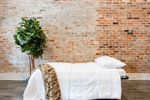 Une pièce avec un mur en briques, un lit avec une literie blanche et une grande plante verte.