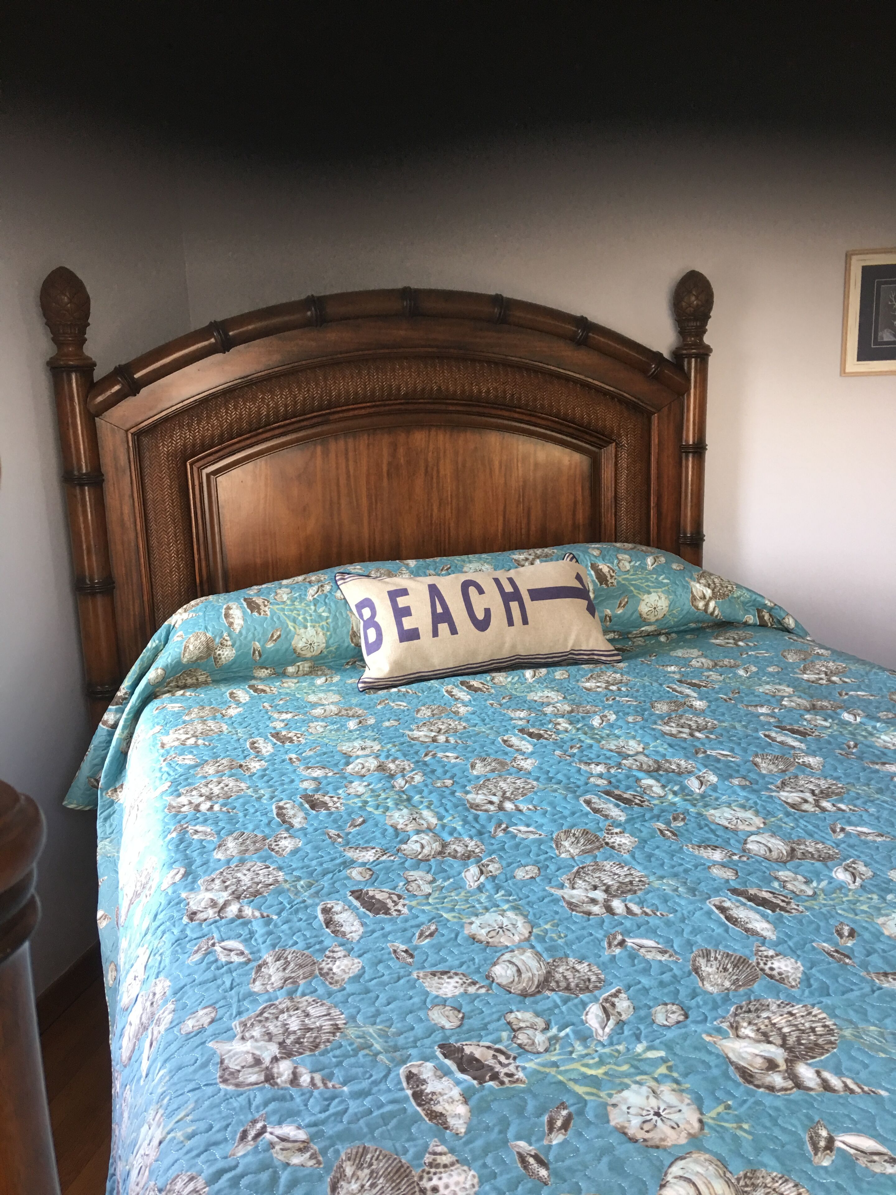 Un lit avec une couette bleue ornée de motifs de coquillages et un oreiller sur lequel est écrit le mot « PLAGE ».