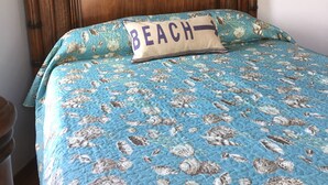 Un letto con una coperta azzurra decorata con conchiglie e un cuscino con la scritta "BEACH".