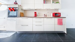 A modern kitchen with white cabinetry, a black tiled floor, a red coffee maker, and a red microwave. - Les Cerisiers - Triplex 3 bedrooms in the center of Namur (Namur)
