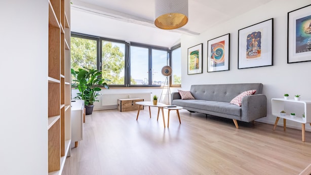 A modern living room with a grey sofa, a coffee table, and a bookshelf. There are large windows and a view of the outside. - Les Cerisiers - Triplex 3 bedrooms in the center of Namur (Namur)