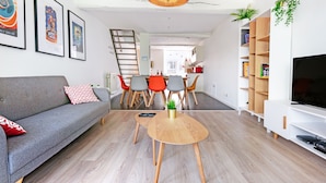 A modern living room with a sofa, coffee table, and TV stand. There is a dining area with chairs and a table, and a kitchen in the background. - Les Cerisiers - Triplex 3 bedrooms in the center of Namur (Namur)