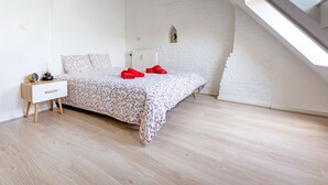 A bedroom with a bed, a nightstand, a small window, and a sloped ceiling. - Les Cerisiers - Triplex 3 bedrooms in the center of Namur (Namur)