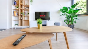 A modern living room with a wooden coffee table, a remote control, a bookshelf, a TV displaying 'NETFLIX', and potted plants. - Les Cerisiers - Triplex 3 bedrooms in the center of Namur (Namur)