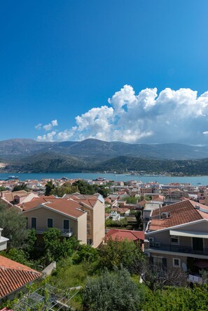 Eine Küstenstadt mit Häusern mit Terrakotta-Dächern, wolkenlosem, blauem Himmel und Blick auf das Meer und die Berge in der Ferne.