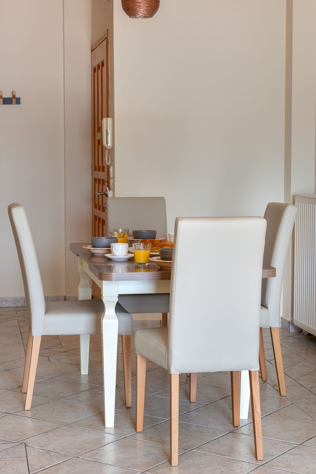 A dining area with a wooden table, four chairs, and a breakfast setting including a bowl, mug, and glass of orange juice.