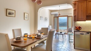 Eine moderne Küche mit Essbereich, ausgestattet mit einem großen Esstisch, gedeckt für ein Frühstück, mit Blick auf das Meer und einem Geschirrspüler.
