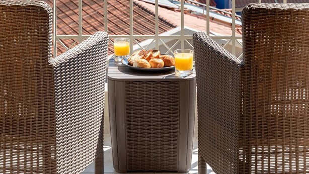 Ein Balkon mit Korbstühlen, einem Tisch mit Frühstück und Blick auf einen See und Gebäude.