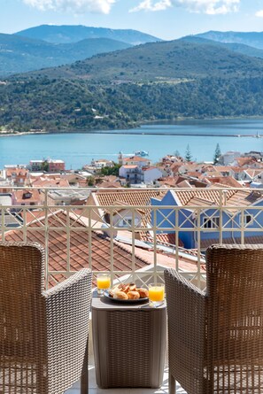 Un balcon avec des fauteuils en osier, une table où est servi le petit-déjeuner, et une vue sur un lac et des bâtiments.