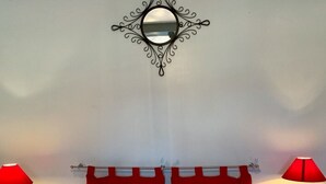 Une chambre à coucher avec un lit, deux tables de chevet, une tête de lit rayée de rouge et de blanc, et un miroir décoratif accroché au mur.