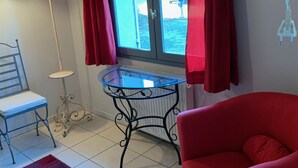 Une pièce avec une chaise rouge, une petite table, une lampe et une fenêtre avec des rideaux.