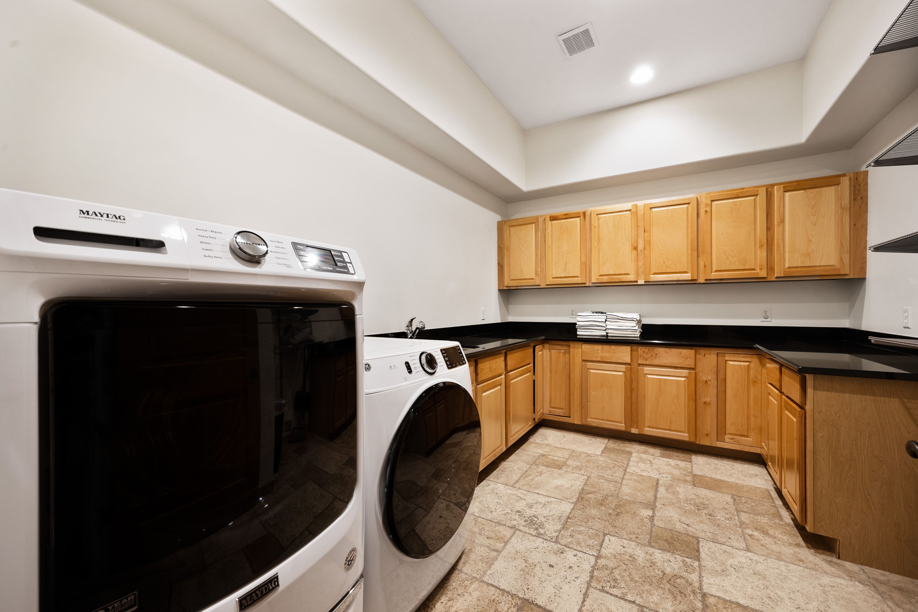 Une cuisine moderne équipée d’un lave-linge et d’un sèche-linge Maytag à chargement frontal, de meubles de rangement en bois et d’un plan de travail noir.