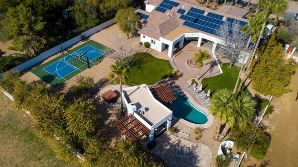 Vue aérienne d’une propriété résidentielle dotée d’un court de tennis, d’une piscine et de panneaux solaires.