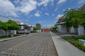 A residential street with modern houses, a paved walkway, and a car parked on the side. - Jaco Beach Condo Vereda B2 (Jacó)