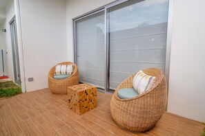 A balcony with two wicker chairs, a small wooden stool, and a large sliding glass door. - Jaco Beach Condo Vereda B2 (Jacó)