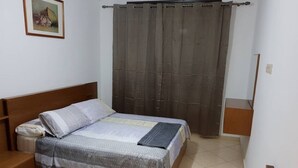 Un dormitorio con cama de madera, mesita de noche y un cuadro enmarcado en la pared, además de una cortina.