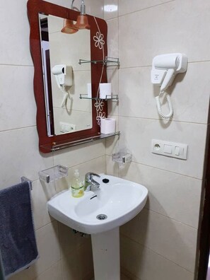 Een badkamer met een witte wasbak, een spiegel met bloemendecoratie, een haardroger en een telefoon.