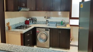 Cocina compacta con armarios de madera oscura, lavadora integrada, estufa a gas y refrigerador de acero inoxidable.