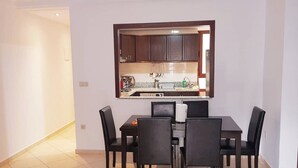 Un comedor con mesa y sillas, una cocina con armarios y encimera, y piso de baldosas.