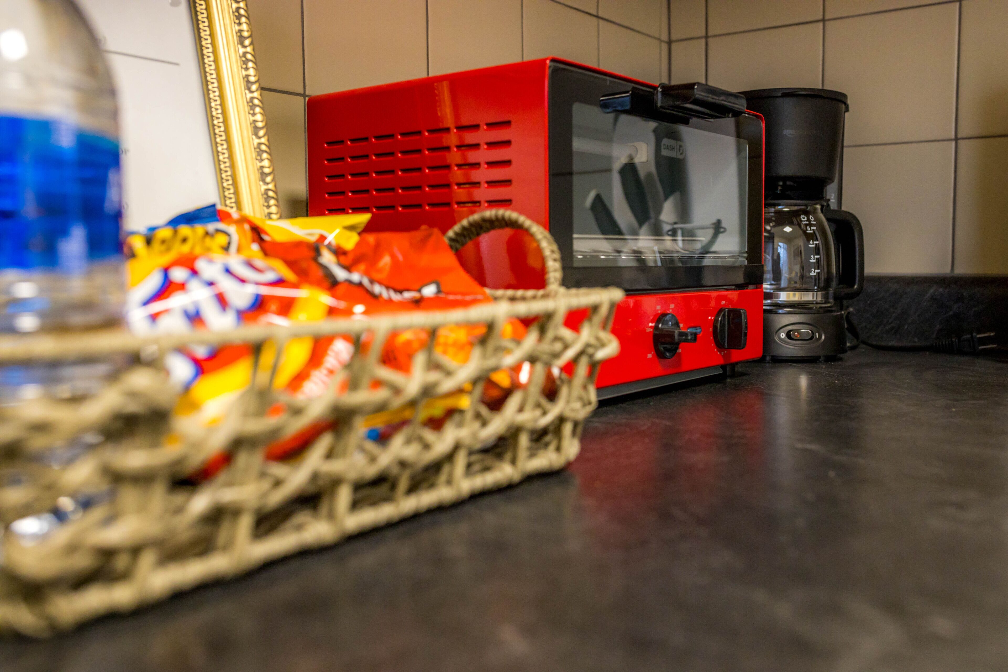 Eine rote Kaffeemaschine steht auf einer Küchenarbeitsplatte neben einer Snack-Auswahl.