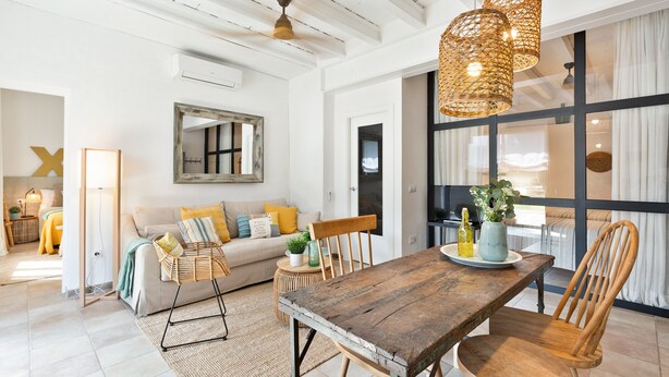 A spacious living room with a wooden dining table, wicker chairs, and a large window with curtains. - Sant Mori- La Escala Boutique apartment (Sant Mori)