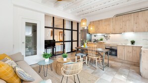 A modern kitchen with wooden cabinets, a dining area with a table and chairs, and a living room with a sofa and a TV. - Sant Mori- La Escala Boutique apartment (Sant Mori)